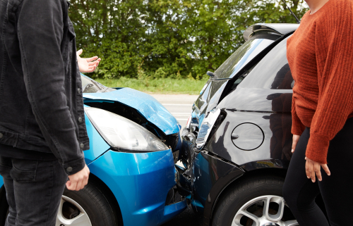 Two people discussing in front of their cars after a collision, showing visible damage to both vehicles.