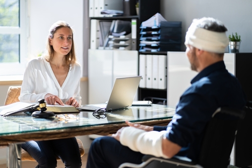 A male patient with head and arm injuries consulting with a female doctor in a bright office.