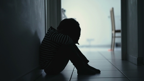 Silhouette of a young child sitting alone in a dimly lit hallway, symbolizing sadness and isolation.