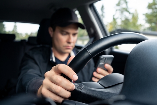 A man driving a car while distracted by his smartphone.