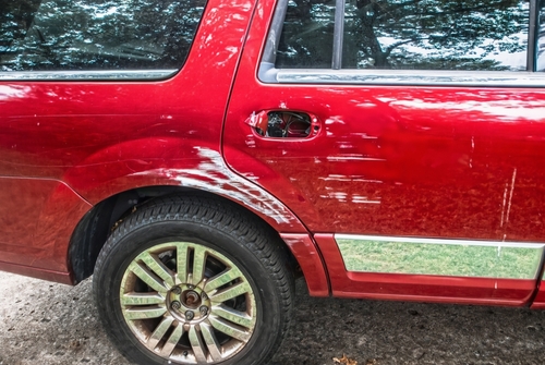 A red SUV with visible scrape marks and damage on its side, parked outdoors near trees.