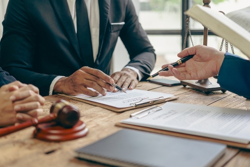 "Lawyer and clients discussing and signing documents at a wooden table, with a legal balance scale and gavel in the foreground, highlighting a legal consultation.