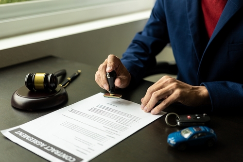 A car accident attorney in a blue suit signing a legal document with a gavel and a car key on the table, symbolizing legal action following a vehicle incident.