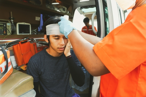 A paramedic applying a head bandage to a young man in an ambulance, indicating immediate medical care after an accident.