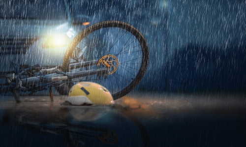 A bicycle and helmet lying on a wet road at night, illuminated by the headlights of a car, symbolizing a rainy night accident scene.