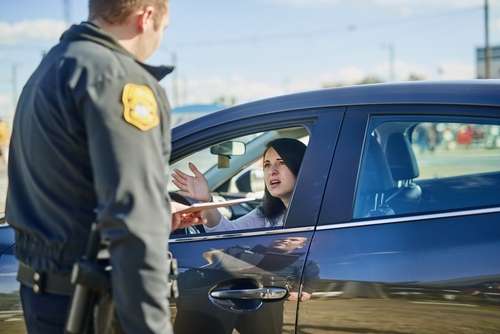 A female driver handing documents to a police officer during a traffic stop, with expressions of concern on her face.