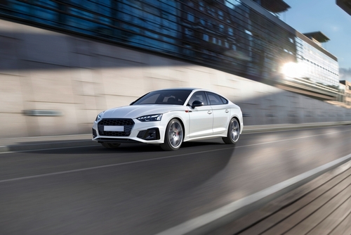 A white sports sedan speeding along a modern city roadway, emphasizing motion and speed.