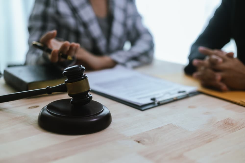 Two individuals discussing legal documents at a desk with a gavel and notepad in focus.