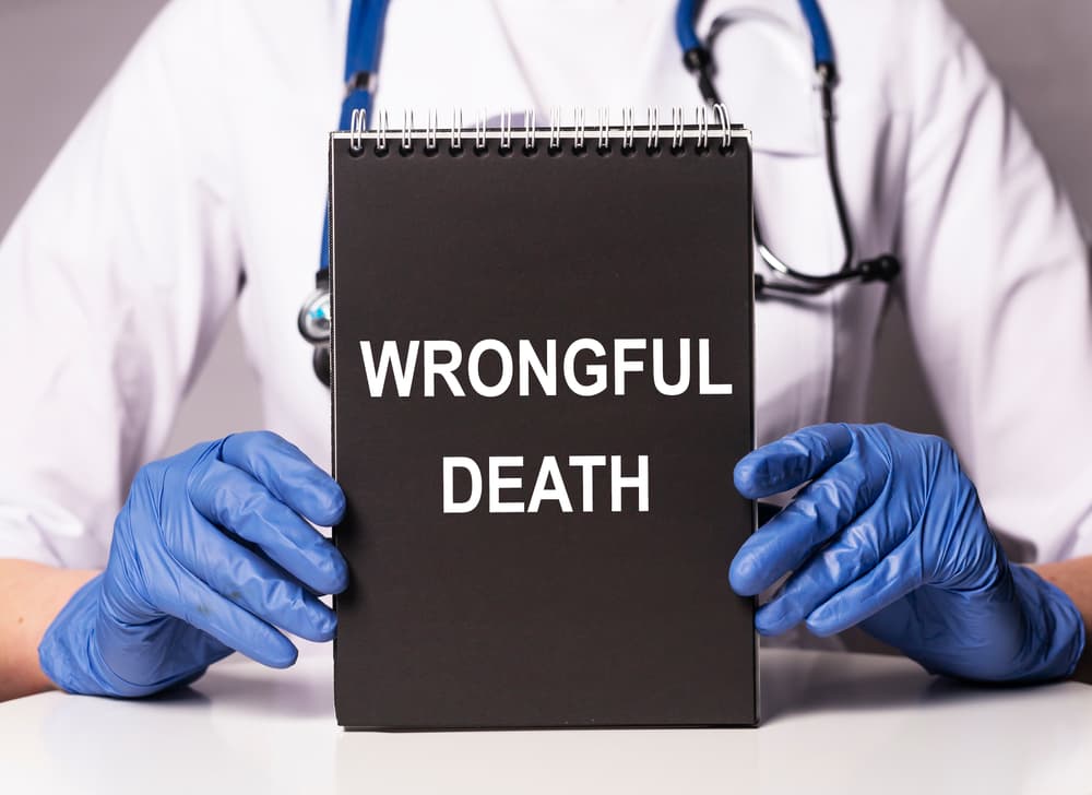 A doctor wearing gloves holds a notebook with "Wrongful Death" written on the cover.