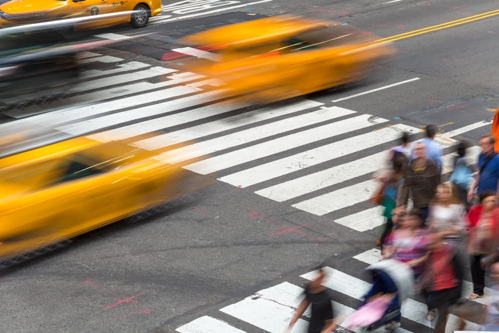 A busy crosswalk with blurred pedestrians and fast-moving yellow taxis in a city intersection.